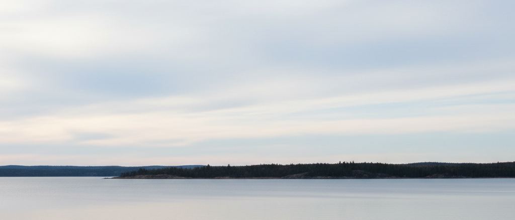 The far shore of a wide lake, a thin dark band between water and sky
