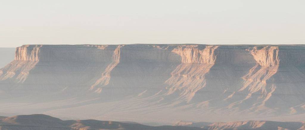 The far rim of a plateau across a wide empty basin, layered in haze